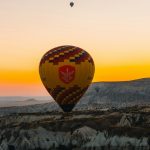 Hot air balloons float over rocky landscape at sunrise.